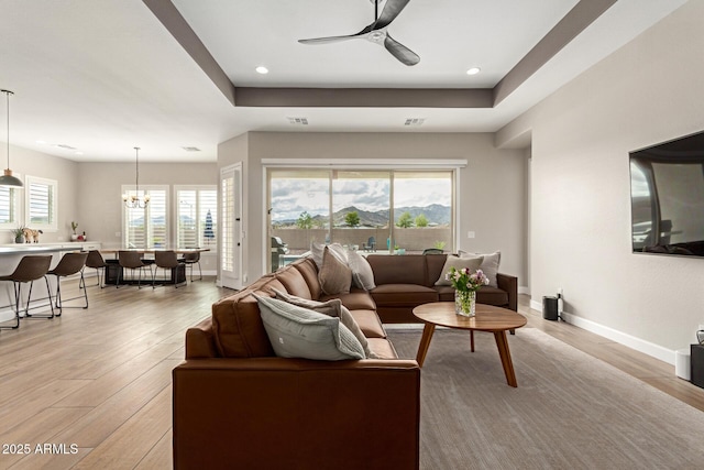 living area featuring baseboards, recessed lighting, light wood-style flooring, ceiling fan with notable chandelier, and a raised ceiling