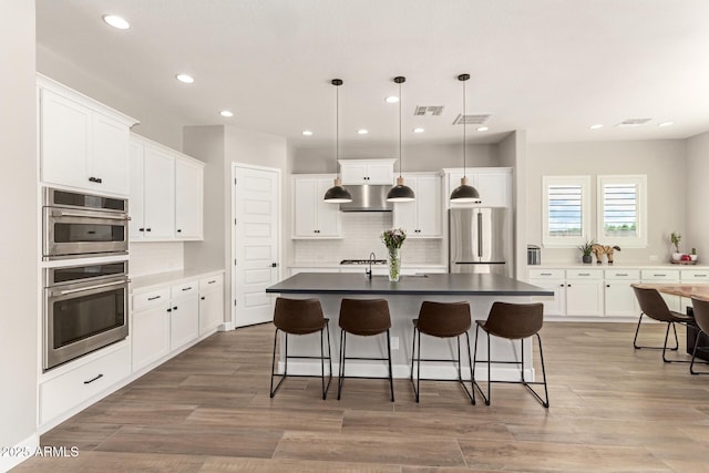 kitchen featuring visible vents, under cabinet range hood, a breakfast bar area, decorative backsplash, and appliances with stainless steel finishes