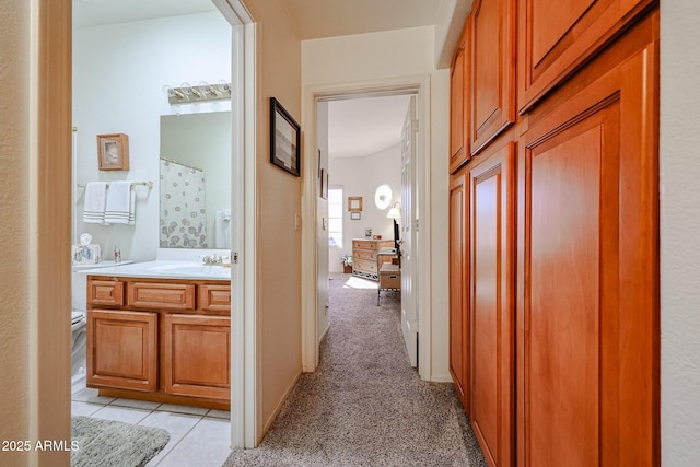 hall with light colored carpet, a sink, baseboards, and light tile patterned floors