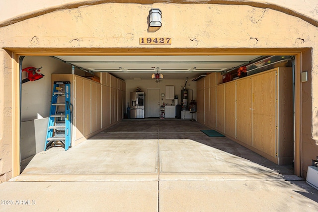 garage featuring gas water heater, washing machine and clothes dryer, a garage door opener, concrete driveway, and water heater