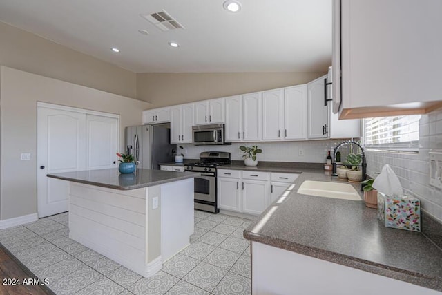 kitchen with sink, a kitchen island, lofted ceiling, white cabinets, and appliances with stainless steel finishes