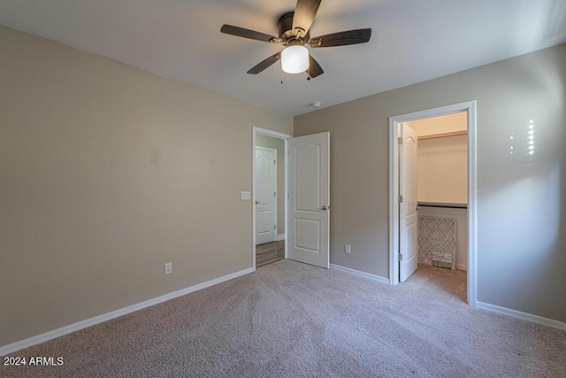 unfurnished bedroom with light carpet, a walk in closet, a closet, and ceiling fan