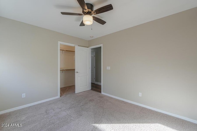 unfurnished bedroom with a walk in closet, ceiling fan, a closet, and light colored carpet