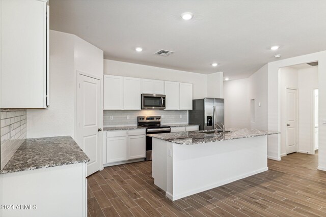 kitchen featuring white cabinetry, a kitchen island with sink, light stone counters, and appliances with stainless steel finishes