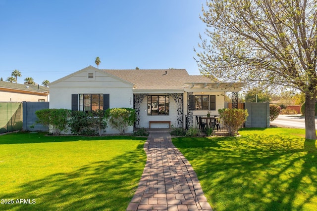 view of front facade featuring a shingled roof, fence, a front lawn, and stucco siding