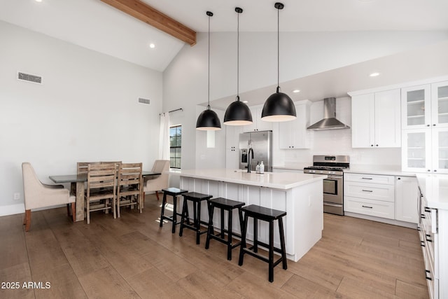 kitchen featuring light wood finished floors, visible vents, appliances with stainless steel finishes, wall chimney range hood, and an island with sink