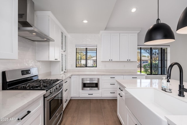 kitchen with white cabinets, dark wood-style floors, stainless steel appliances, wall chimney range hood, and a sink