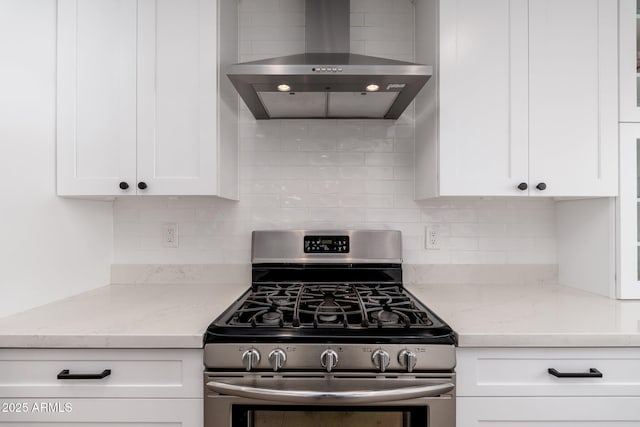 kitchen with light stone counters, tasteful backsplash, gas stove, white cabinetry, and wall chimney exhaust hood