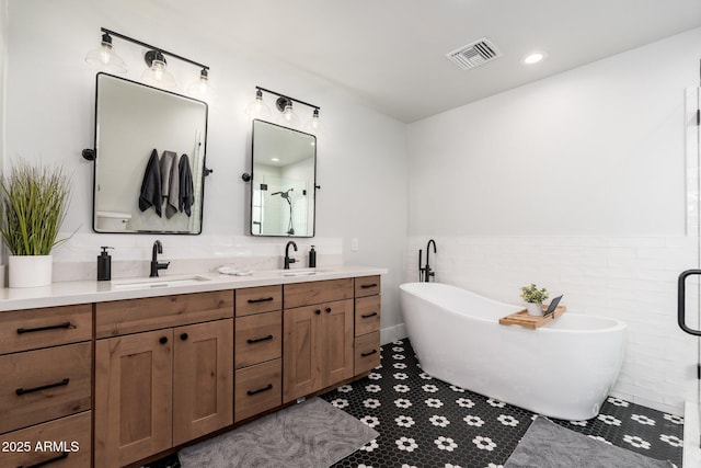 bathroom featuring tile walls, double vanity, visible vents, a freestanding bath, and a sink