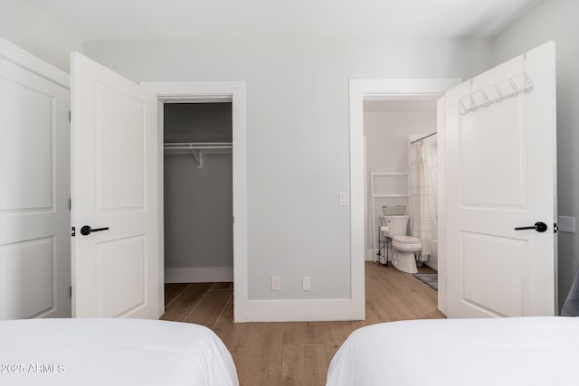 bedroom with a closet, a spacious closet, baseboards, and wood finished floors