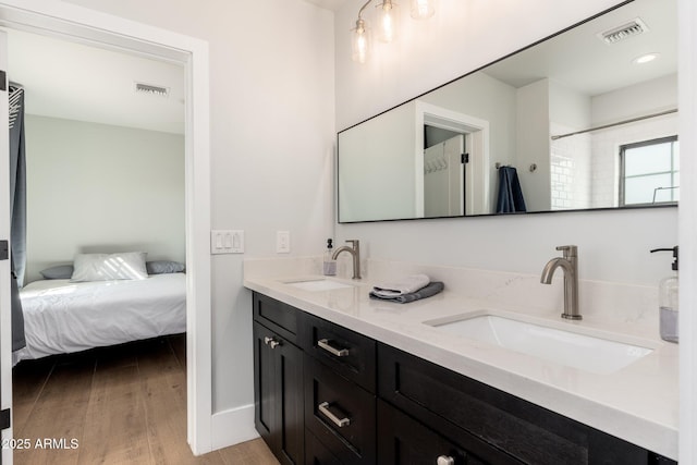 ensuite bathroom featuring visible vents, a sink, ensuite bathroom, and wood finished floors