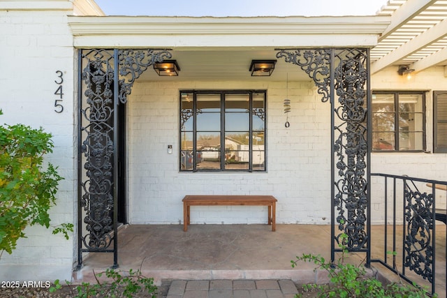 doorway to property featuring a porch, brick siding, and a pergola