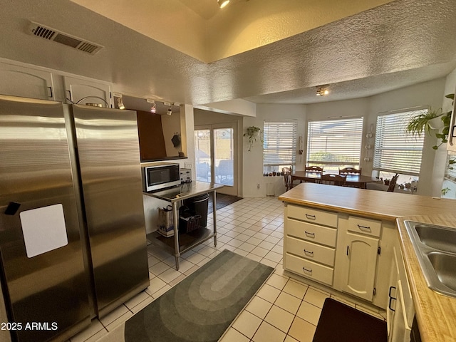 kitchen featuring a wealth of natural light, light tile patterned floors, a textured ceiling, and stainless steel refrigerator