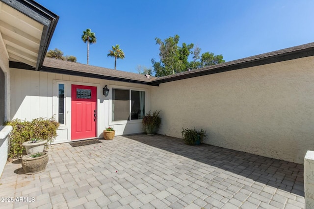 doorway to property featuring a patio area and roof with shingles