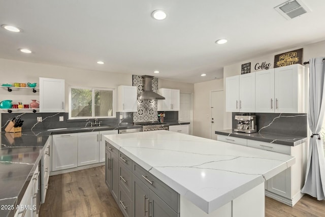 kitchen featuring visible vents, a sink, wood finished floors, a center island, and wall chimney exhaust hood