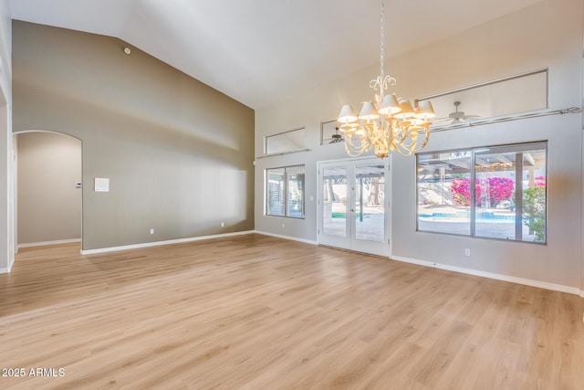 empty room with light wood-type flooring, vaulted ceiling, a healthy amount of sunlight, and a notable chandelier