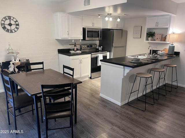 kitchen with stainless steel appliances, kitchen peninsula, dark hardwood / wood-style floors, sink, and white cabinetry