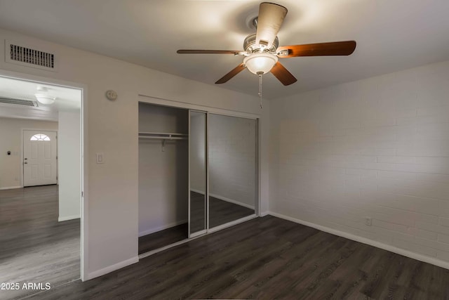 unfurnished bedroom with a closet, ceiling fan, brick wall, and dark wood-type flooring