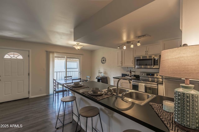 kitchen featuring white cabinets, appliances with stainless steel finishes, dark hardwood / wood-style flooring, sink, and a breakfast bar area