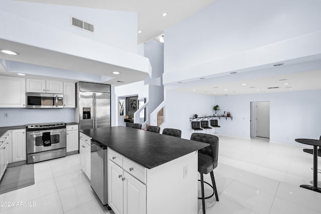 kitchen featuring appliances with stainless steel finishes, a kitchen bar, light tile patterned floors, white cabinets, and a center island