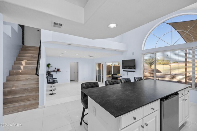 kitchen with white cabinets, a breakfast bar area, light tile patterned flooring, a kitchen island, and stainless steel fridge