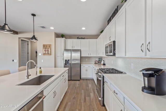 kitchen featuring pendant lighting, white cabinets, sink, light hardwood / wood-style flooring, and appliances with stainless steel finishes