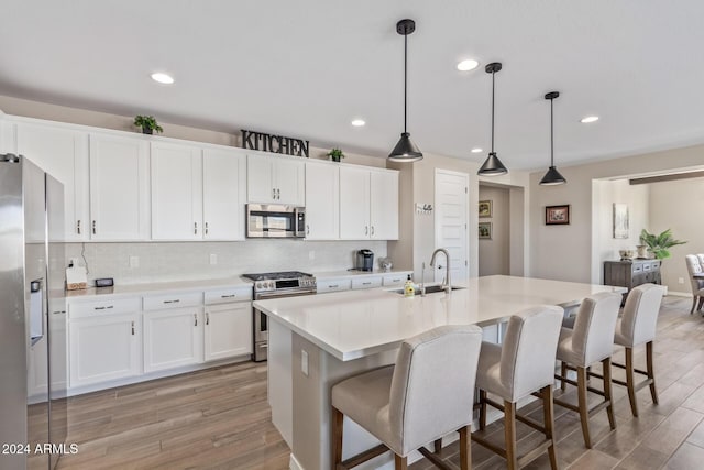 kitchen featuring pendant lighting, stainless steel appliances, a kitchen island with sink, and light hardwood / wood-style floors