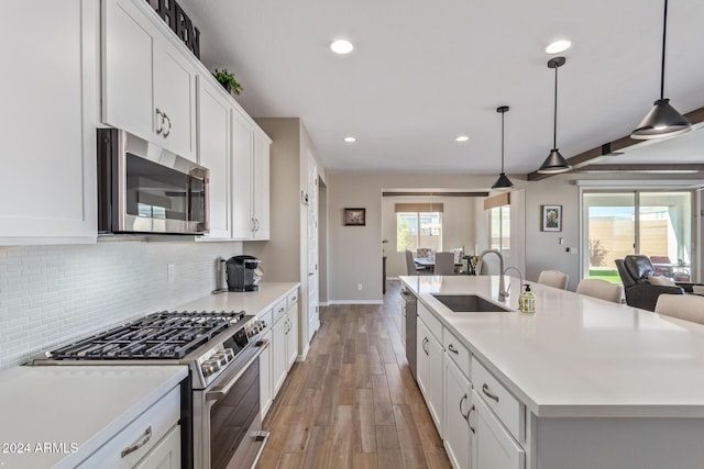 kitchen featuring a kitchen island with sink, hanging light fixtures, sink, light hardwood / wood-style floors, and stainless steel appliances