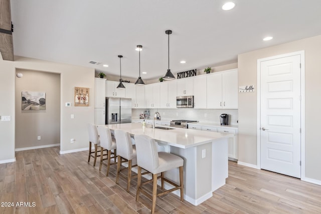 kitchen with white cabinets, decorative light fixtures, a kitchen island with sink, and appliances with stainless steel finishes