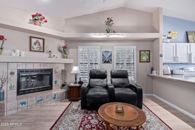 living area with lofted ceiling, baseboards, wood finished floors, and a tile fireplace