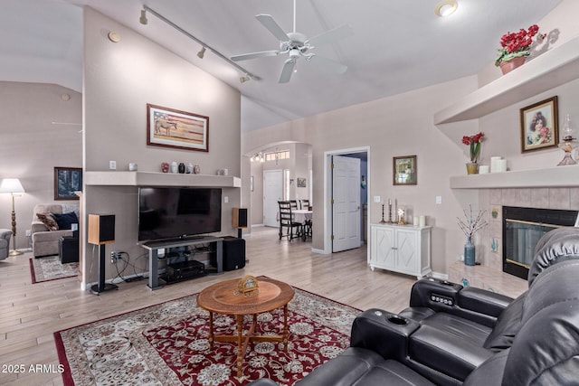 living room featuring arched walkways, light wood finished floors, a fireplace, and a ceiling fan