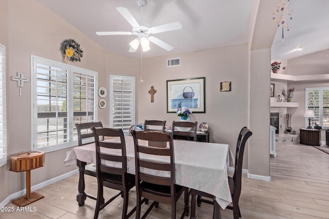 dining area featuring baseboards, visible vents, a ceiling fan, a glass covered fireplace, and light wood-type flooring