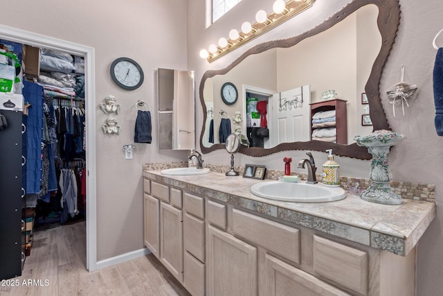 bathroom with double vanity, wood finished floors, a sink, and a walk in closet