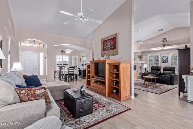 living area featuring light wood finished floors, visible vents, arched walkways, ceiling fan, and high vaulted ceiling