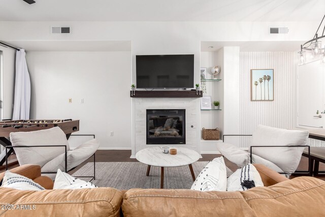 living area with a glass covered fireplace, visible vents, baseboards, and wood finished floors