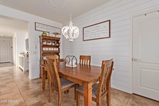 dining room featuring a chandelier, light tile patterned floors, and wooden walls