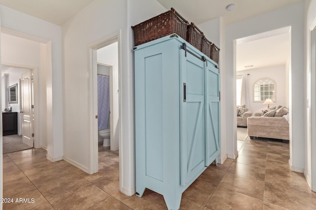 hall featuring baseboards and light tile patterned flooring