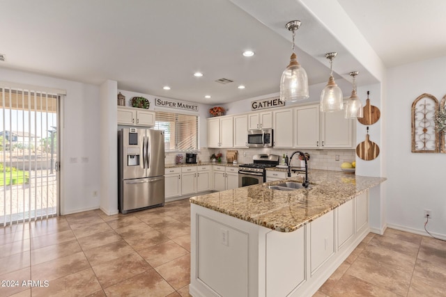 kitchen featuring appliances with stainless steel finishes, a sink, a peninsula, decorative backsplash, and light stone counters