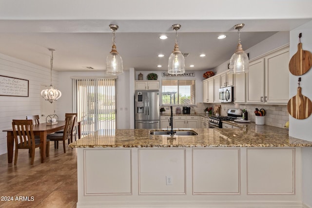 kitchen with appliances with stainless steel finishes, a sink, light stone counters, a peninsula, and decorative backsplash