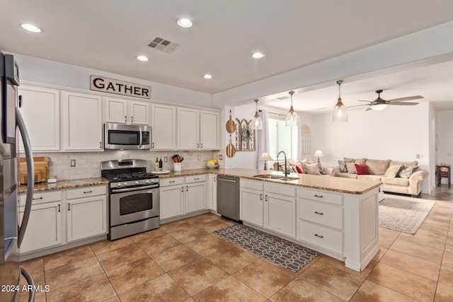 kitchen with appliances with stainless steel finishes, a sink, a peninsula, open floor plan, and decorative backsplash