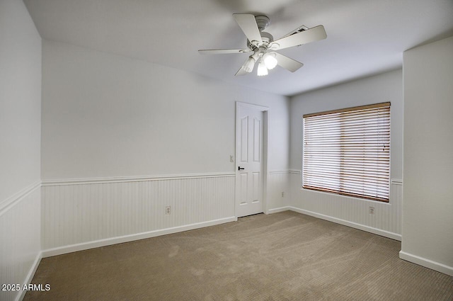 spare room featuring wainscoting, carpet, and ceiling fan