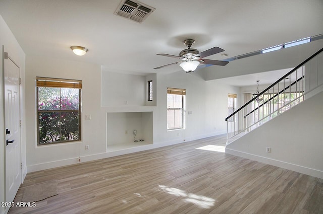 unfurnished living room featuring visible vents, ceiling fan, stairway, a wealth of natural light, and light wood-style flooring