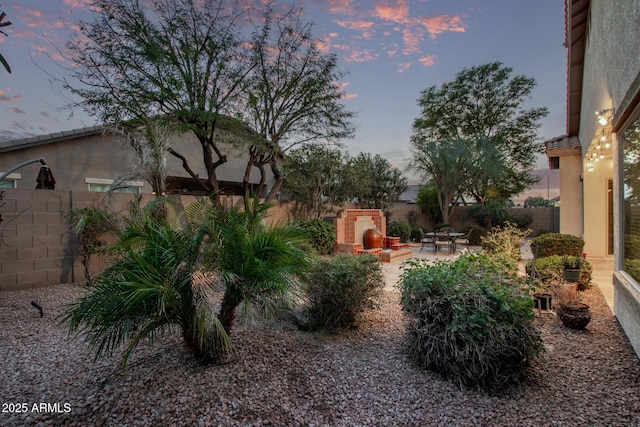 yard at dusk with exterior fireplace and a patio