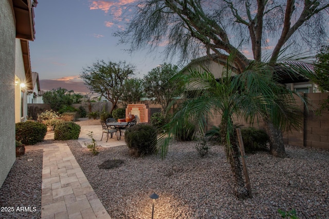 yard at dusk featuring exterior fireplace and a patio area