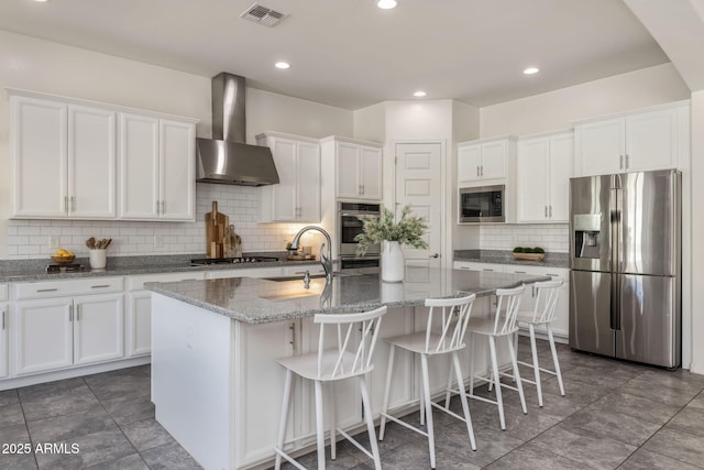 kitchen with sink, white cabinetry, stainless steel appliances, a kitchen island with sink, and wall chimney range hood