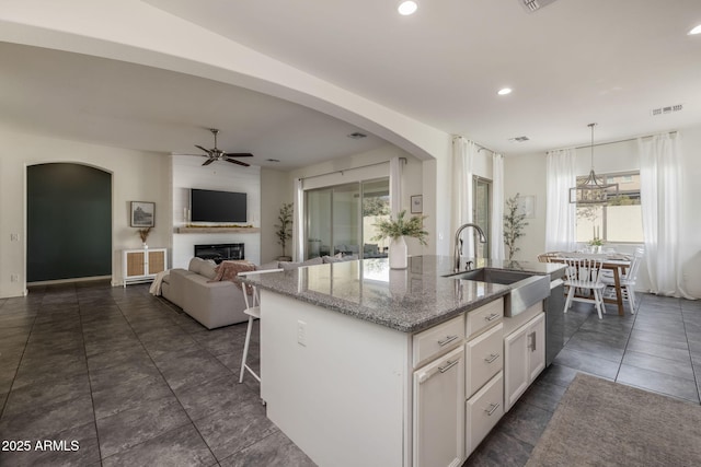 kitchen featuring stone counters, white cabinetry, sink, hanging light fixtures, and a kitchen island with sink