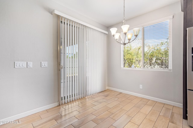 empty room with a chandelier, light hardwood / wood-style flooring, and a healthy amount of sunlight