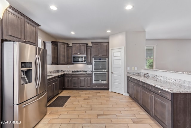 kitchen featuring light stone countertops, appliances with stainless steel finishes, dark brown cabinets, and light wood-type flooring