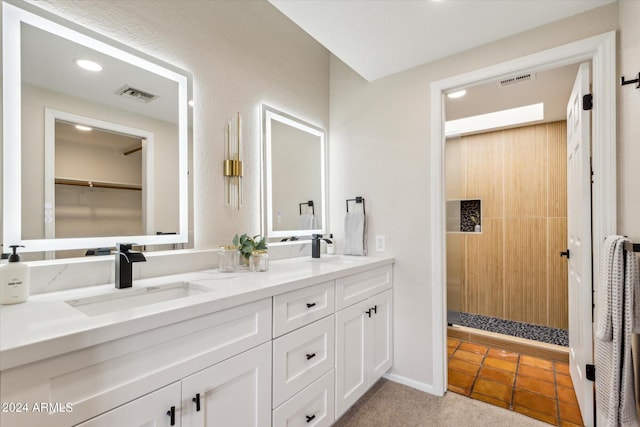 full bath with a tile shower, double vanity, a sink, and visible vents