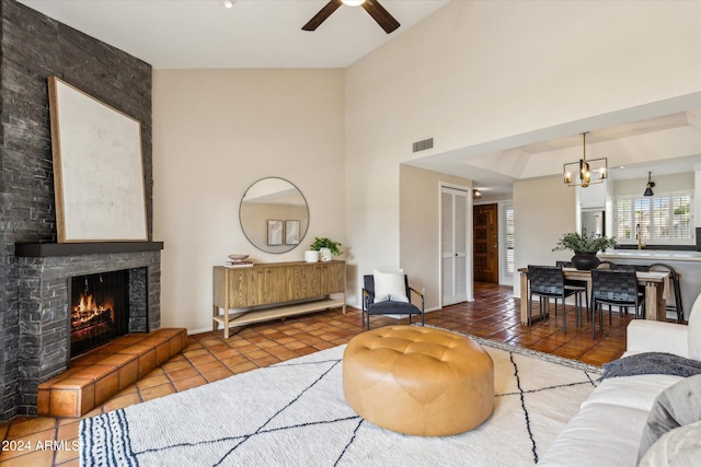 tiled living room with lofted ceiling, a tiled fireplace, ceiling fan with notable chandelier, and a raised ceiling